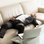 Tired businessman lying relaxed on sofa. Man fall asleep on couch in office when stayed at work till late. Entrepreneur takes short break, recovery sleep after too much hard work at project on laptop